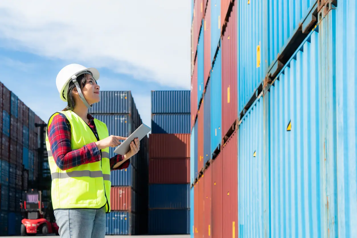 engineer woman or foreman manager in container depot working with digital tablet for control and checking industrial container yard for logistics oversea import export shipping business in port.